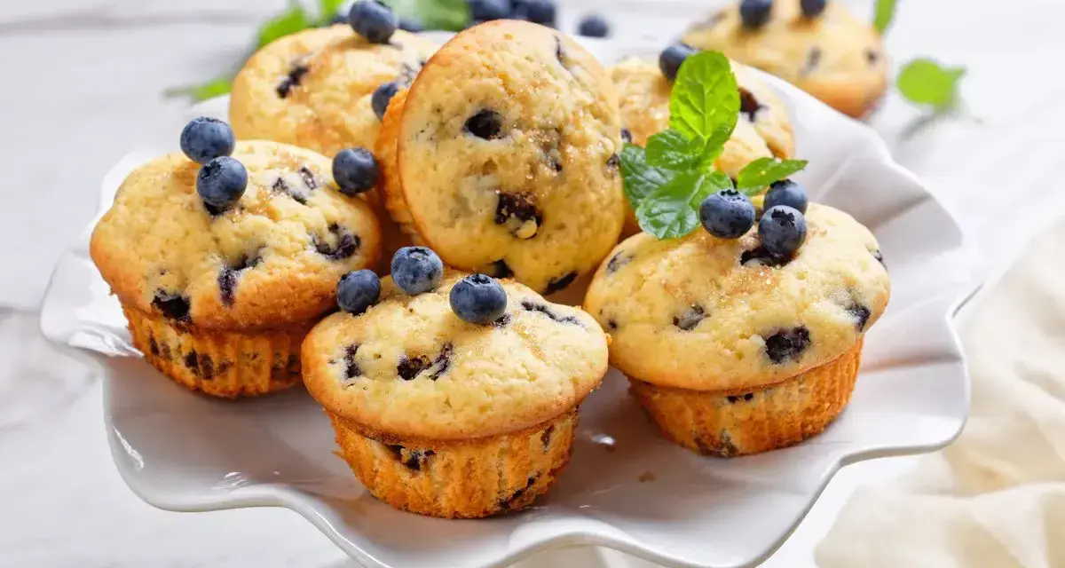 Muffin ai mirtilli appena sfornati, decorati con mirtilli freschi e menta. Una deliziosa ricetta per iniziare la giornata.