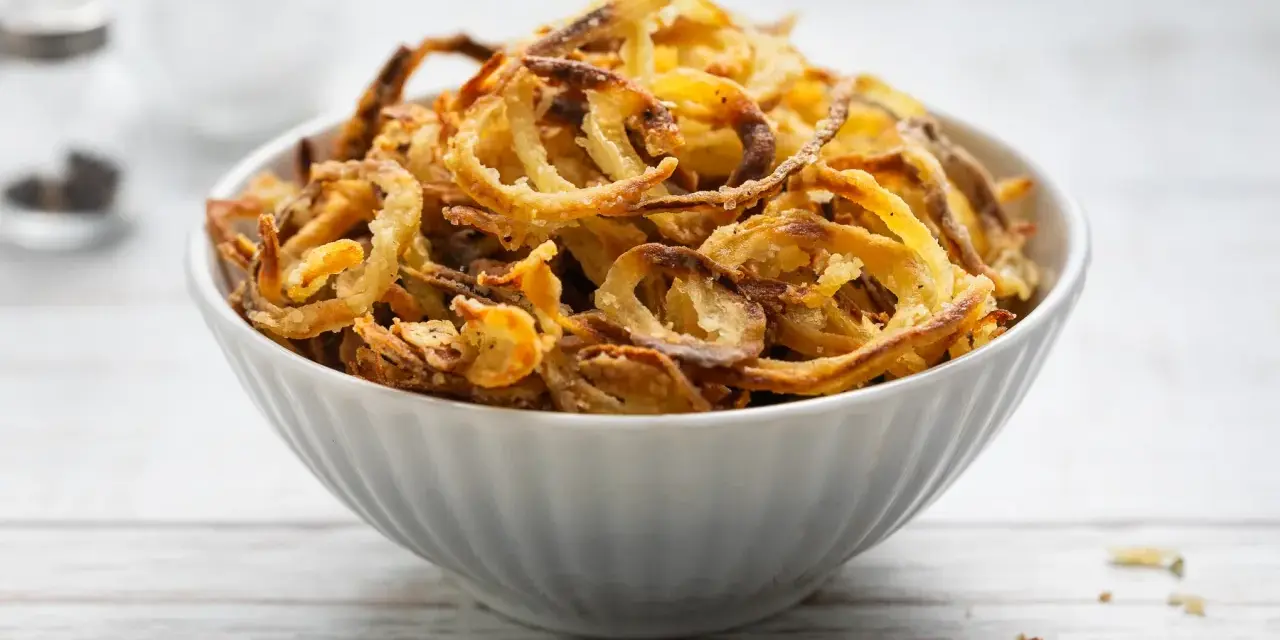 Ciotola piena di croccanti cipolle fritte dorate, perfette per accompagnare ogni piatto.