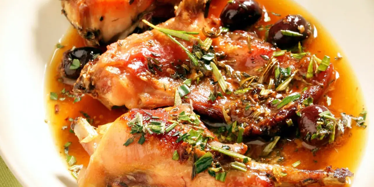 Coniglio alla ligure succulento, con olive nere e erbe aromatiche, immerso in un sugo dorato.