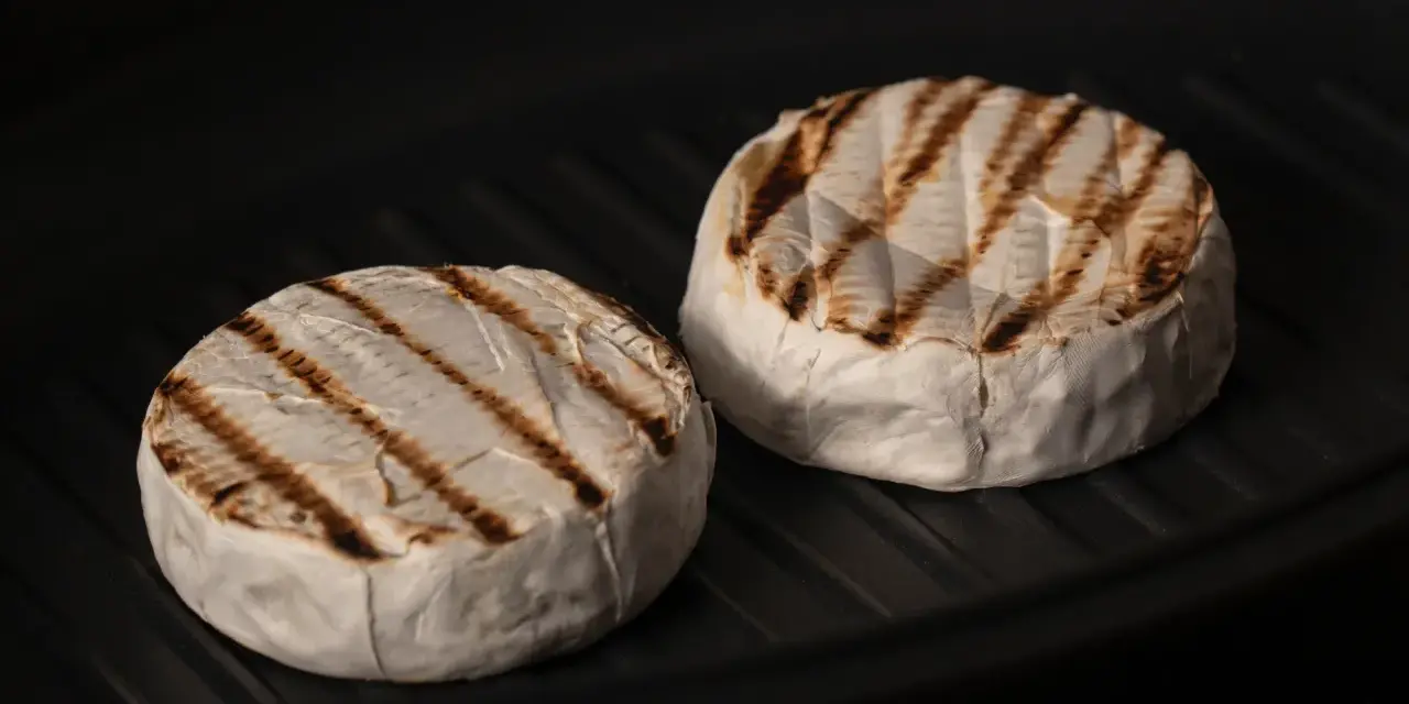 Due forme di formaggio da fare alla piastra, con belle striature dorate, cuociono in una padella scura.