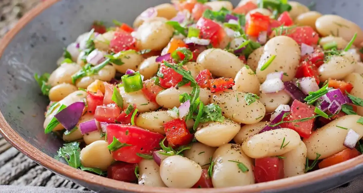 Insalata di fagioli bianchi, pomodori freschi, cipolla rossa e erbe aromatiche in una ciotola rustica. Un piatto colorato e salutare.