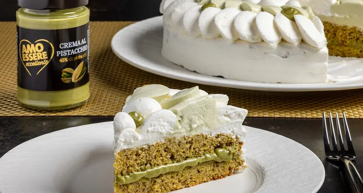 Una fetta di torta soffice al pistacchio, con crema al pistacchio e panna montata. Accanto, un barattolo di crema al pistacchio.