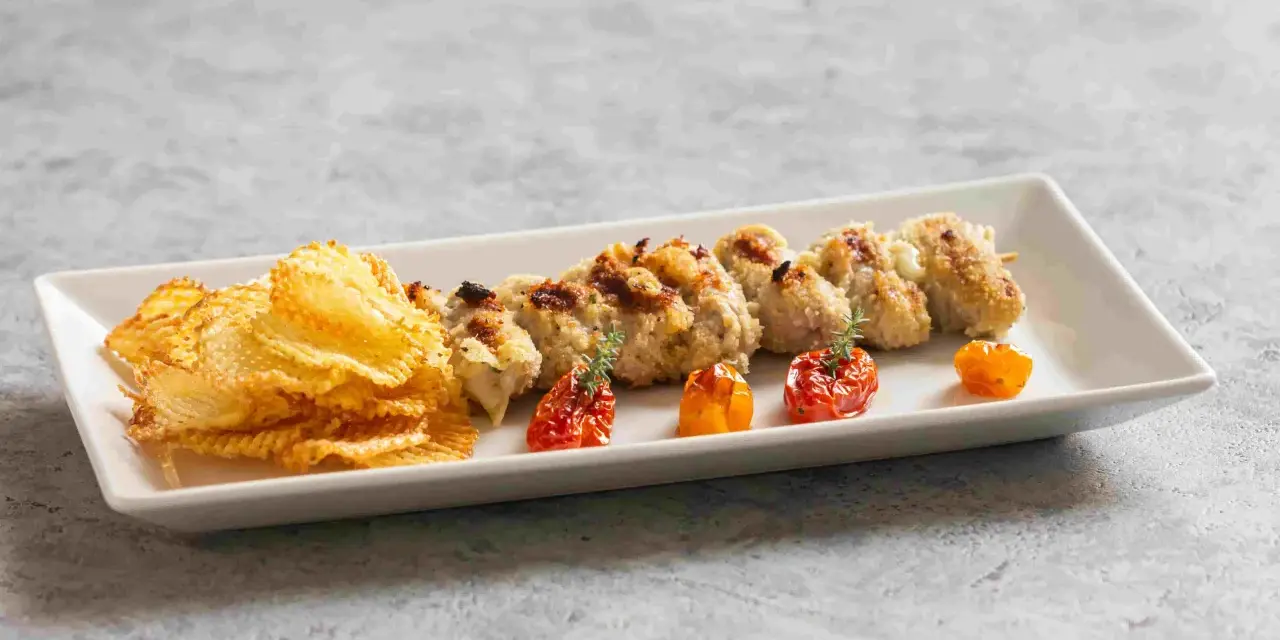 Involtini alla messinese su uno spiedino, accompagnati da patatine croccanti e pomodorini confit.