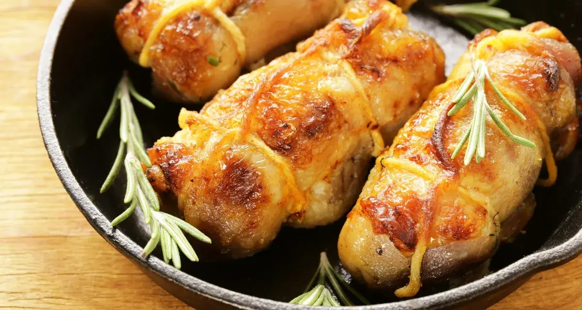 Involtini di pollo al forno dorati e succulenti, legati con spago da cucina e guarniti con rametti di rosmarino fresco, serviti in una padella di ghisa.