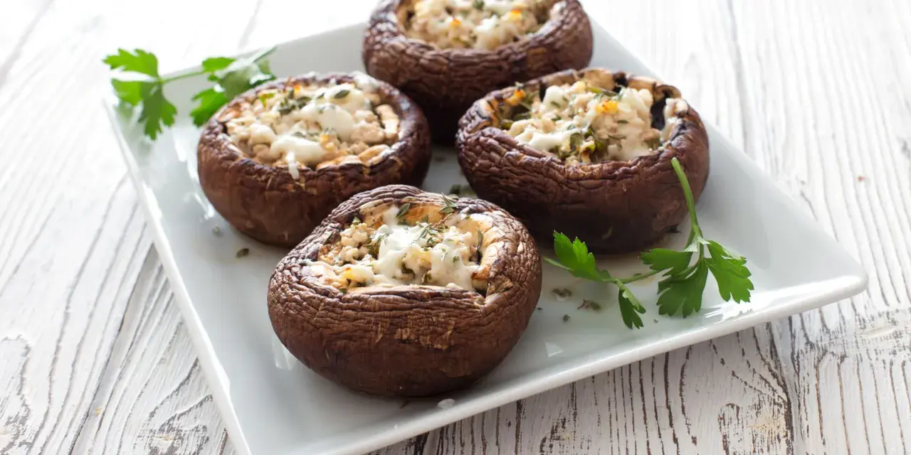 Quattro funghi ripieni al forno, dorati e invitanti, guarniti con prezzemolo fresco su un piatto bianco.