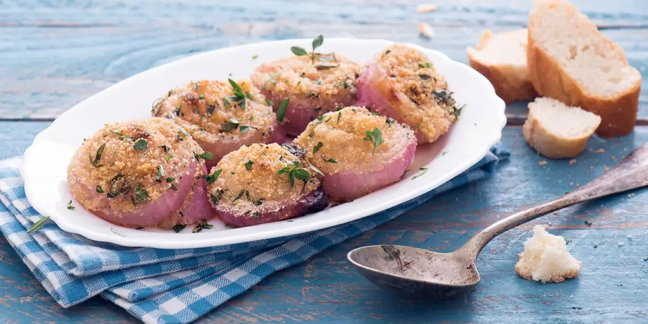 Deliziose cipolle al forno, dorate e profumate, servite su un piatto bianco con pane croccante e un cucchiaio d'argento.