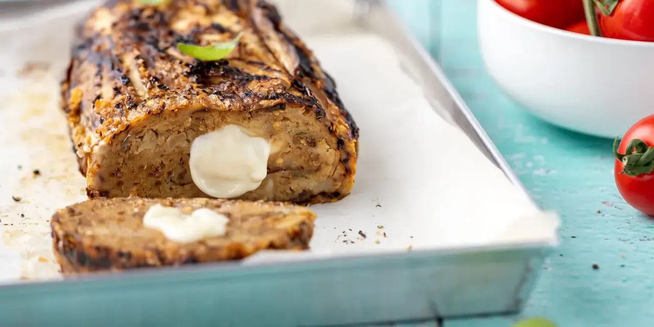 Polpettone di melanzane grigliato, ripieno di formaggio filante, su teglia con basilico e pomodorini.