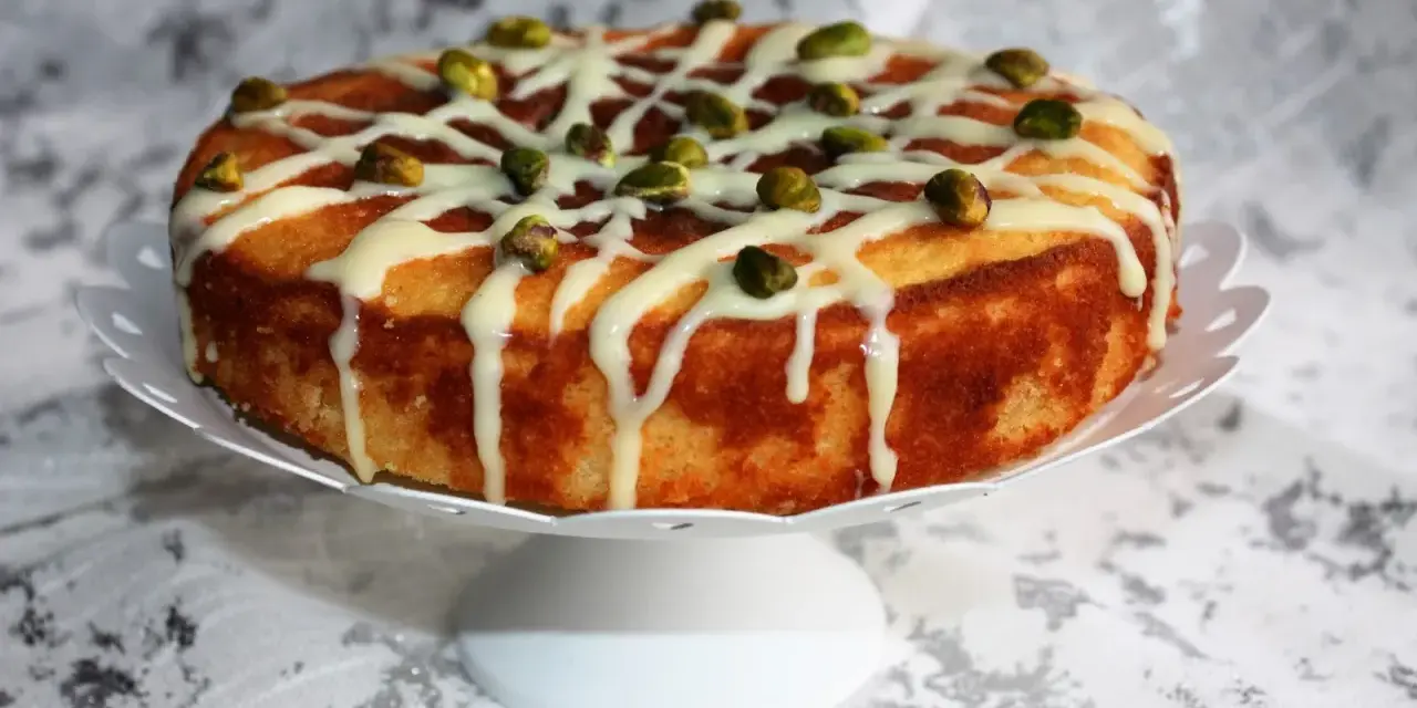 Deliziosa torta al bergamotto, decorata con glassa bianca e pistacchi croccanti, pronta per essere gustata.