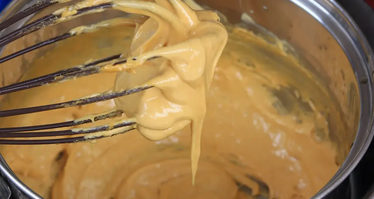 Una frusta raccoglie una crema densa e dorata, pronta per diventare uno zabaione freddo.