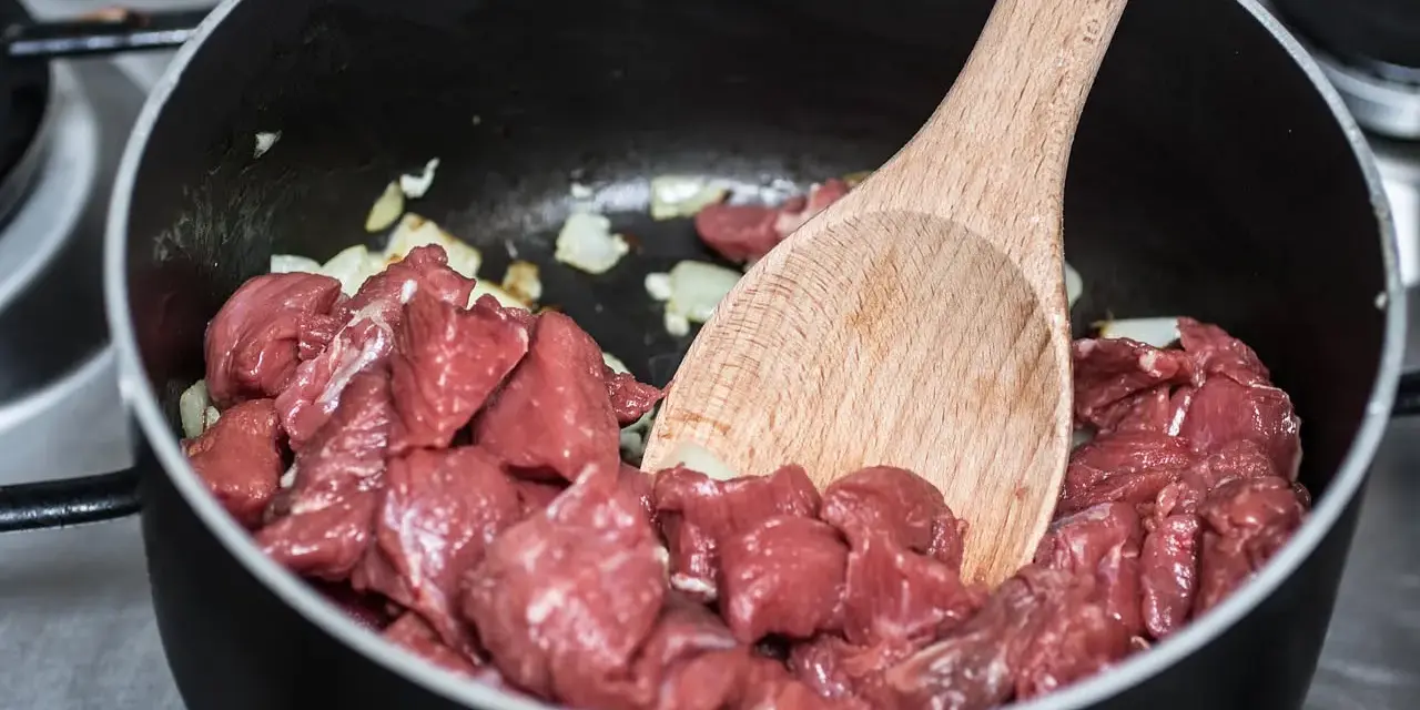 Bocconcini di manzo crudo in padella con cipolla, pronti per diventare uno spezzatino gommosa di manzo.