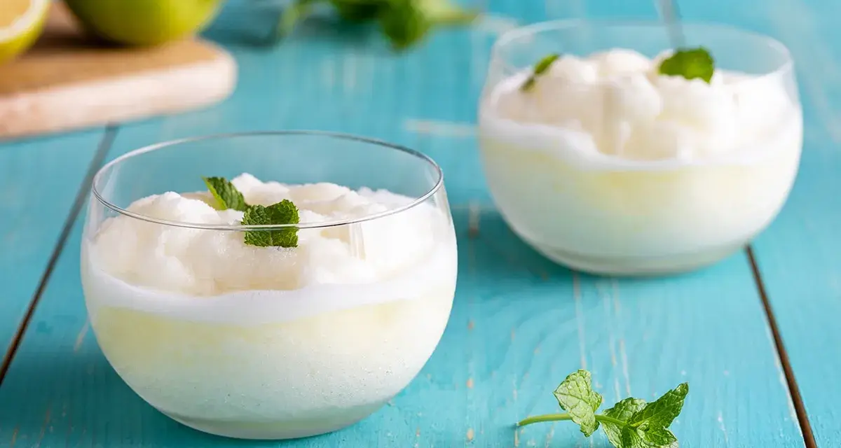 Sorbetto al limone senza gelatiera: due coppette di fresco sorbetto al limone guarnite con menta, su un tavolo di legno blu.