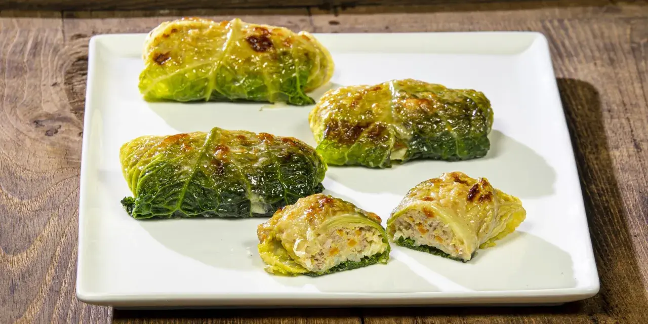 Cinque capunet piemontesi, involtini di verza ripieni, serviti su un piatto bianco.