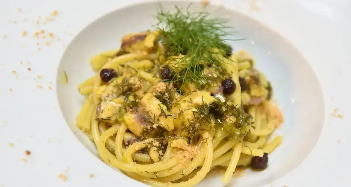 Un piatto invitante di pasta con finocchi, olive e acciughe, guarnito con erbe fresche e pangrattato.