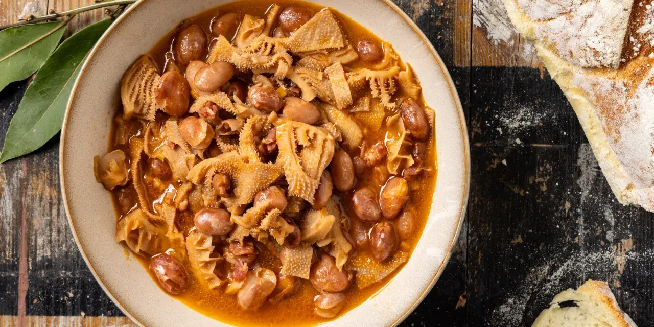 Piatto fumante di trippa alla milanese con fagioli, su un tavolo di legno rustico, accanto a pane casereccio.