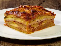 Una fetta di parmigiana di patate, stratificata con formaggio e salumi, servita su un piatto bianco.
