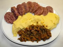 Piatto con fette di cotechino o musetto, polenta gialla e lenticchie stufate.