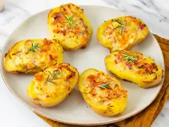 Patate ripiene al forno, dorate e gratinate, guarnite con rosmarino fresco. Un piatto invitante e saporito.