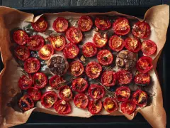 Pomodori al forno, caramellati e succosi, con aglio arrostito e rosmarino su carta forno.