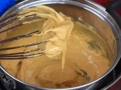 Una frusta raccoglie una crema densa e dorata, pronta per diventare uno zabaione freddo.