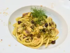 Un piatto invitante di pasta con finocchi, olive e acciughe, guarnito con erbe fresche e pangrattato.