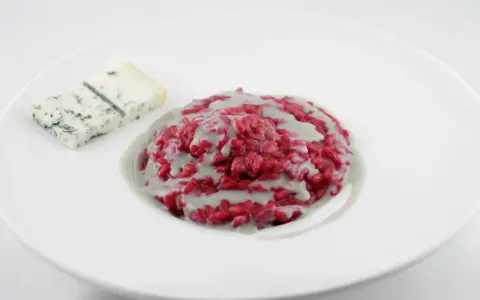 Risotto barbabietola e gorgonzola, un piatto vibrante e saporito, con una fetta di formaggio blu accanto.