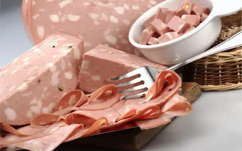 Fetta di mortadella con pistacchi e pepe, servita su un tagliere con fette arrotolate e cubetti in una ciotola.