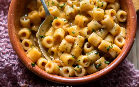 Una ciotola di terracotta piena di pasta e fagioli saporita, con un cucchiaio che ne raccoglie una porzione.