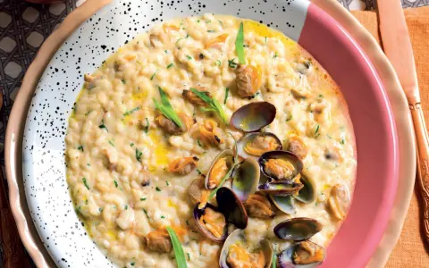 Un cremoso risotto alle vongole, guarnito con prezzemolo tritato e cozze fresche, servito in un piatto bianco a pois.
