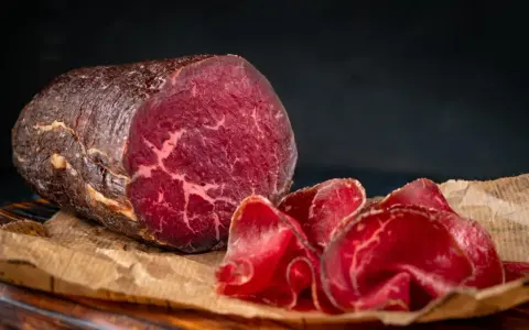 Un pezzo intero e fette sottili di bresaola, con la sua carne rossa e marezzata, evidenziano la differenza tra bresaola e punta d'anca.