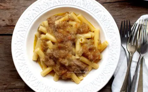 Piatto di pasta con ragù genovese napoletana, servito in un piatto bianco decorato, con forchette d'argento accanto.