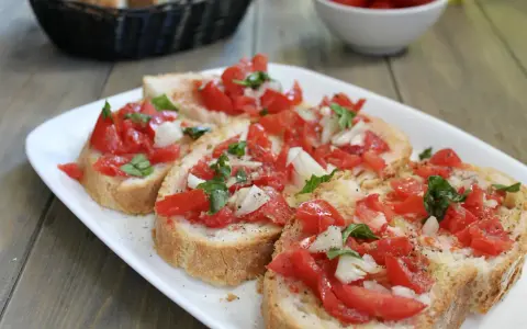 Fette di pane tostato condite con pomodoro fresco, cipolla e basilico, un classico della panzanella romana.