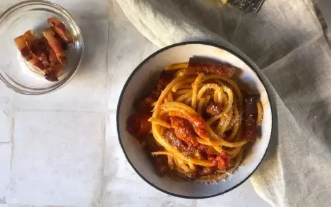 Un piatto invitante di bucatini all'amatriciana, con guanciale croccante e una salsa rossa saporita, spolverato di formaggio grattugiato.