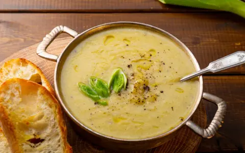 Una ciotola di calda crema di patate, guarnita con erba cipollina e pepe, servita con fette di pane tostato.