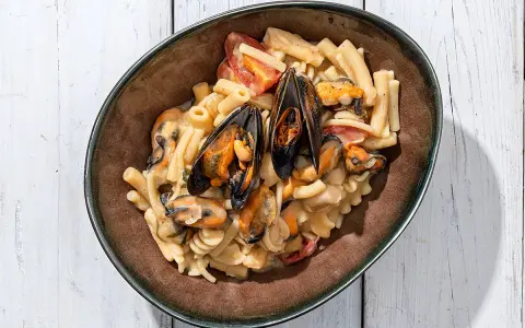 Piatto di pasta con fagioli e cozze, condita con pomodorini e una cremosa salsa.