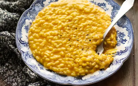 Un cremoso risotto con la zucca, servito su un piatto decorato con un motivo blu e bianco. Un cucchiaio d'argento è immerso nel piatto.