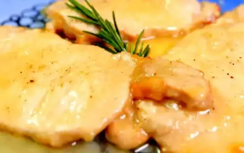 Deliziose scaloppine di maiale in salsa dorata, guarnite con un rametto di rosmarino fresco.