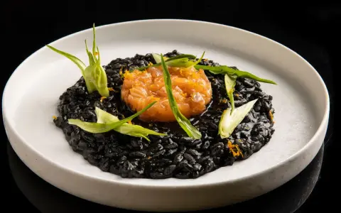 Un piatto di risotto al nero di seppia, guarnito con tartare di salmone e germogli verdi.