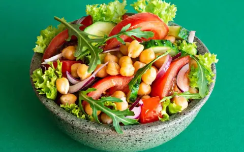 Insalata di ceci colorata con pomodori, cetrioli, cipolla rossa, lattuga e rucola in una ciotola grigia.
