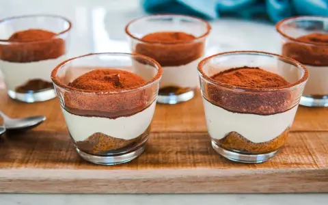 Delizioso tiramisù con pavesini senza uova, servito in bicchierini trasparenti e spolverato di cacao.