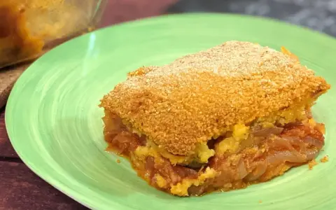 Una fetta di pitta di patate dorata e croccante, con un ripieno succulento di patate e pomodoro, servita su un piatto verde.