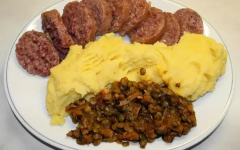 Piatto con fette di cotechino o musetto, polenta gialla e lenticchie stufate.