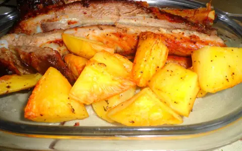 Costine di maiale al forno con patate dorate, un piatto succulento e saporito, pronto per essere gustato.