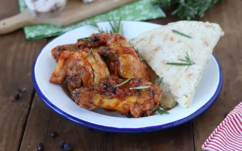 Piatto di friccò di pollo con pomodoro, olive e rosmarino, accompagnato da pane rustico.