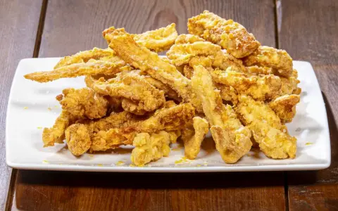 Un mucchio di croccante trippa fritta dorata, cosparsa di scorza di limone, su un piatto bianco.