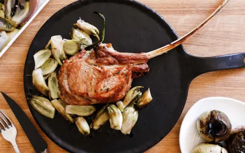Un succulento tomahawk alla griglia, servito con verdure arrosto su un piatto nero.
