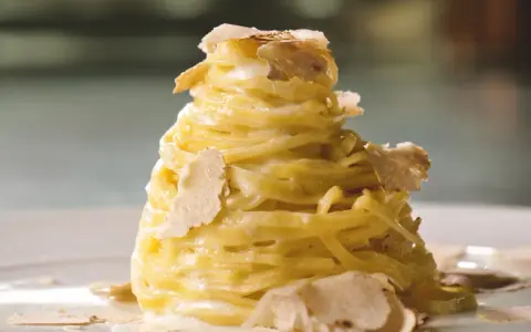 Un nido di pasta al tartufo, condita con una cremosa salsa e guarnita con scaglie sottili di tartufo bianco.