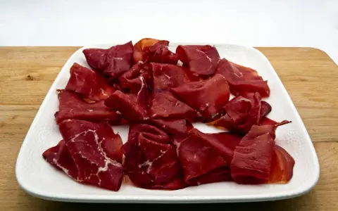 Fetta di bresaola scura, forse di cavallo, su un piatto bianco. Meglio bresaola di cavallo o manzo? La scelta è tua!