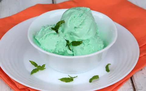 Coppa di cremoso gelato alla menta con latte condensato, guarnito con foglie di menta fresca.