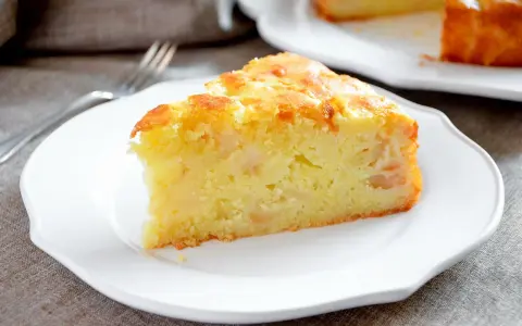 Una fetta di torta margherita con mele, soffice e dorata, servita su un piatto bianco.