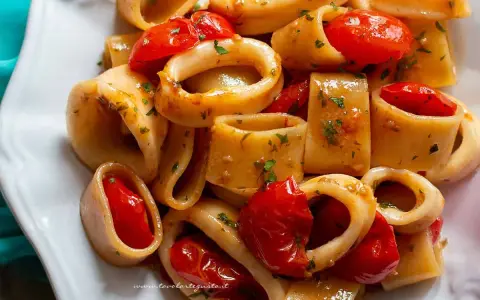 Un piatto invitante di pasta calamarata con pomodorini freschi e prezzemolo tritato, pronto per essere gustato.